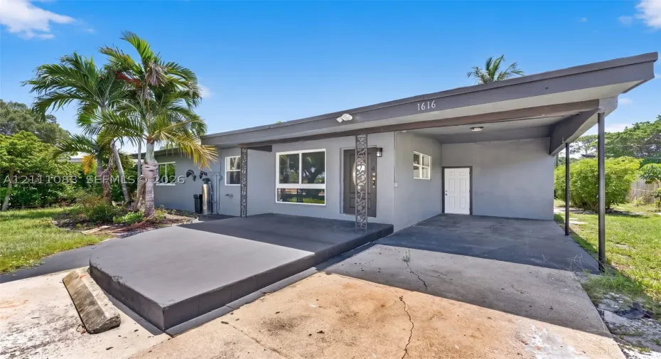 Mid-century modern exterior featuring a flat roofline, attached covered carport, decorative metal porch pillars, and a concrete patio