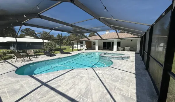 Screened lanai featuring a custom-shaped pool, integrated spa with stone-tile finish, and expansive stone-paver decking