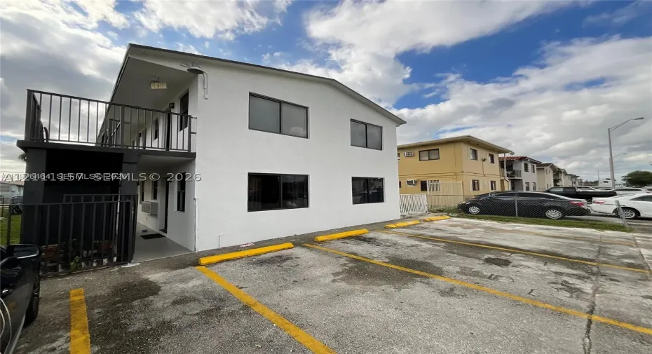 Two-story exterior featuring white stucco finish, second-level metal balcony railing, and designated paved parking area