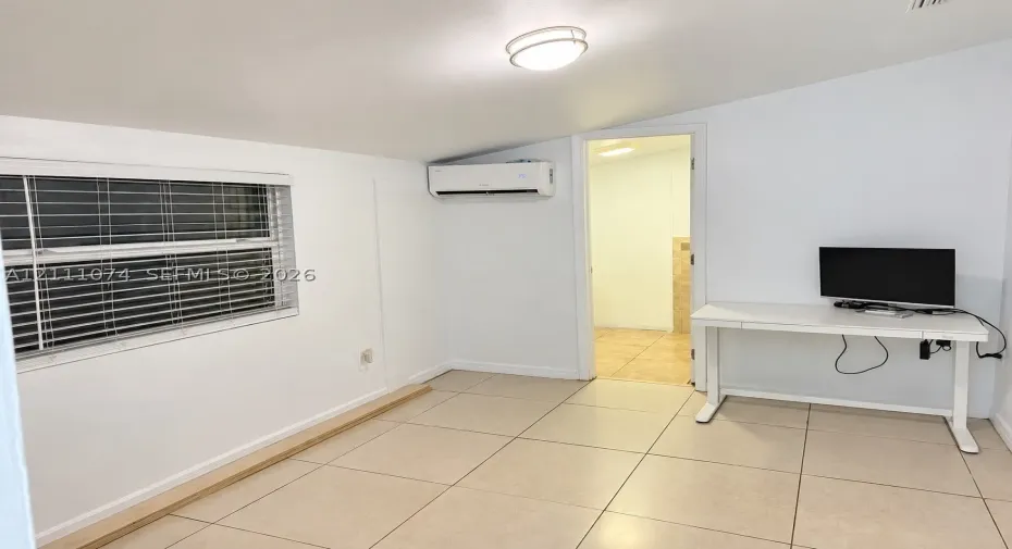Interior room featuring large-format ceramic tile flooring, a mounted ductless mini-split climate control system, a flush-mount ceiling light fixture, and a window with horizontal blinds