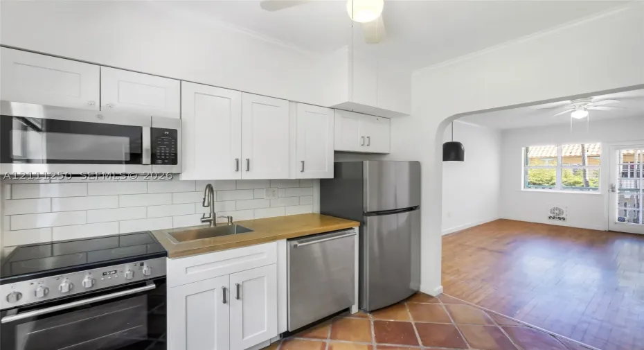 Kitchen featuring white Shaker-style cabinetry, stainless steel appliances, a white subway tile backsplash, a wood-finish countertop, and terracotta tile flooring