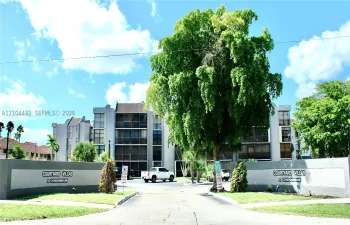 Multi-story condominium exterior featuring stucco facade, recessed private balconies, and established landscaping with mature shade trees