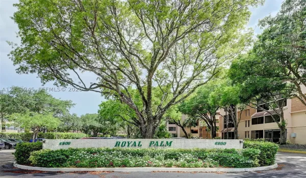 Monument entrance sign with stone-finish base, integrated landscaping, and large mature shade trees