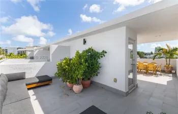 Covered rooftop terrace featuring light-grey tile flooring, white stucco walls, and a glass-paneled exterior door