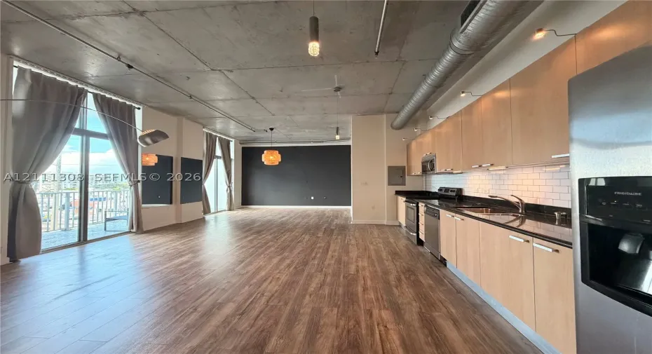 Industrial-style interior featuring exposed concrete ceilings, wood-finish flooring, floor-to-ceiling windows, and a kitchen equipped with flat-panel cabinetry and stone countertops