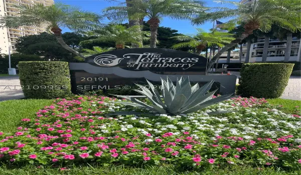 Monument sign for The Terraces at Turnberry featuring polished stone lettering, mature palm trees, sculpted hedges, and landscaped flower beds