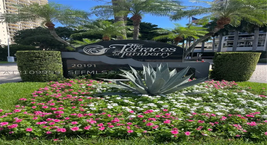 Monument sign for The Terraces at Turnberry featuring polished stone lettering, mature palm trees, sculpted hedges, and landscaped flower beds