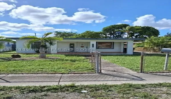 Single-story exterior featuring a covered front porch, concrete walkway, and chain-link perimeter fencing