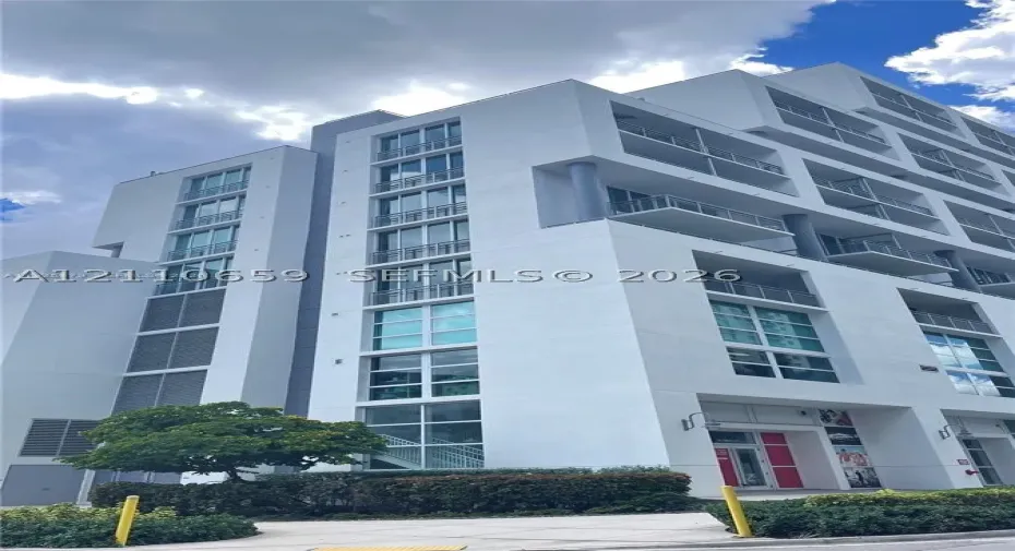 Multi-story building exterior featuring a white facade, floor-to-ceiling glass windows, and private balconies with metal railings