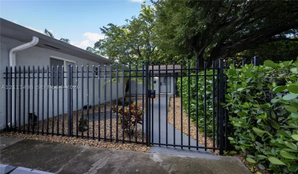 Gated exterior area featuring a concrete walkway, decorative gravel ground cover, and metal perimeter fencing