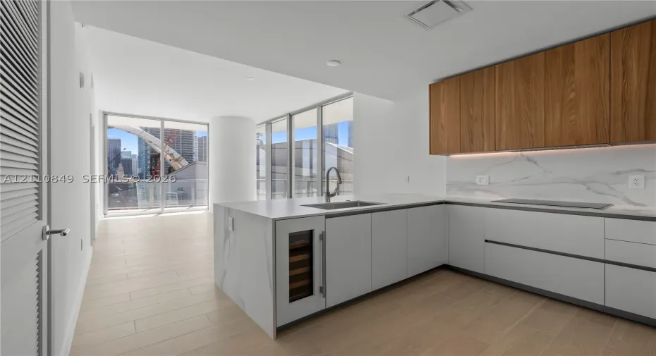 Kitchen featuring slab-surface countertops, integrated wine cooler, light-toned wood-finish flooring, full-height windows, and two-tone flat-panel cabinetry