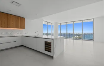 Kitchen featuring flat-panel cabinetry, a stone-surfaced island with an integrated wine refrigerator, large-format tile flooring, and floor-to-ceiling windows