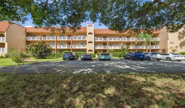 Three-story building exterior featuring a tile roof, stucco facade, and multiple levels of private balconies with white railings