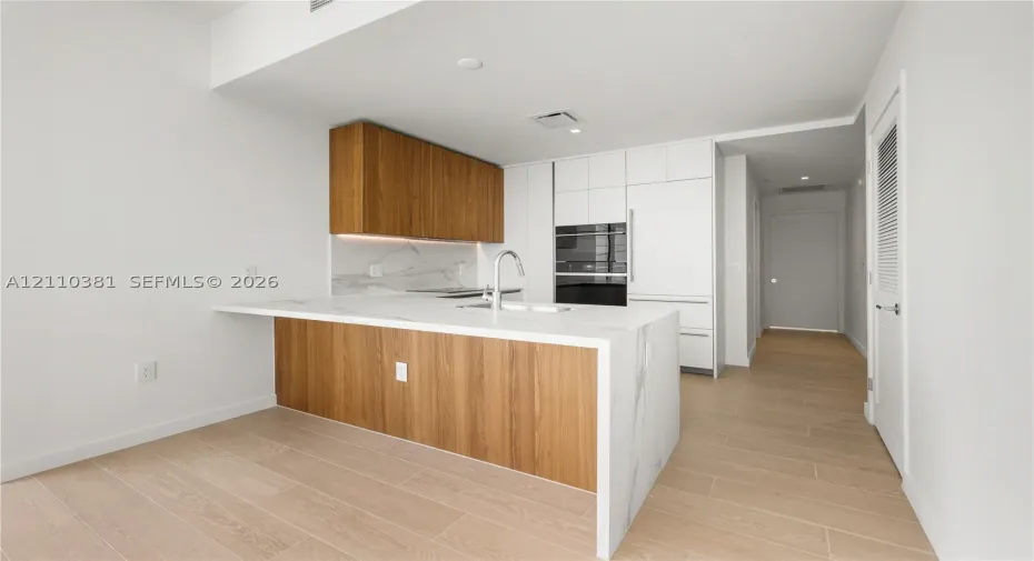 Kitchen featuring wood-finish cabinetry, waterfall-edge countertop, integrated appliance suite, and wood-finish flooring