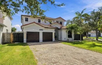 Two-story stucco exterior featuring a tiled roof, paver driveway, and an attached two-car garage