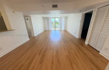 Open-concept interior featuring wood-finish flooring, louvered closet doors, and a glass-paneled sliding door opening to a balcony