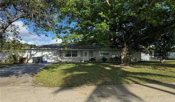 Single-story residence with a concrete driveway, attached garage, covered front porch, and mature trees on the grounds