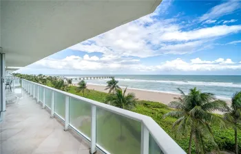 Covered balcony featuring tile flooring and a glass-paneled railing overlooking the ocean, sandy beach, and palm trees