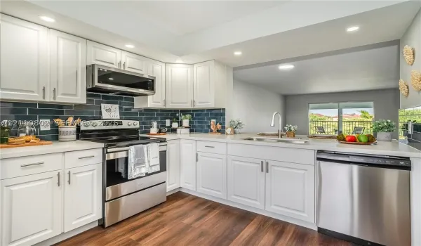 Kitchen featuring white cabinetry, stainless steel appliances, dark tile backsplash, light-toned countertops, and wood-finish flooring