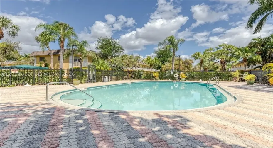 In-ground swimming pool with integrated stair entry, surrounded by patterned stone paver decking and enclosed by black metal perimeter fencing