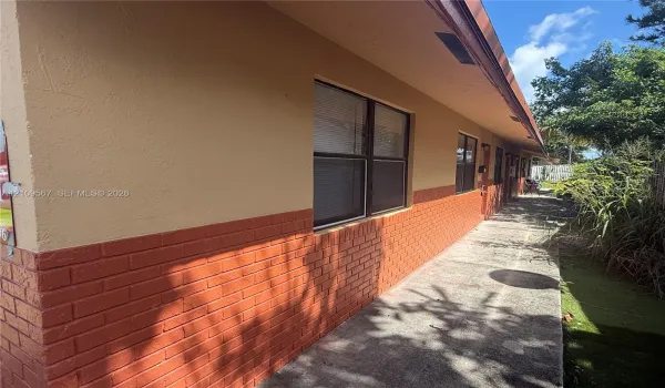 Exterior facade featuring a combination of textured stucco and brick masonry, concrete walkway, and window groupings with dark frames
