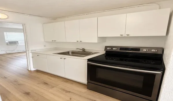 Kitchen featuring white cabinetry, solid-surface countertops, stainless steel sink with metal faucet, and black electric range