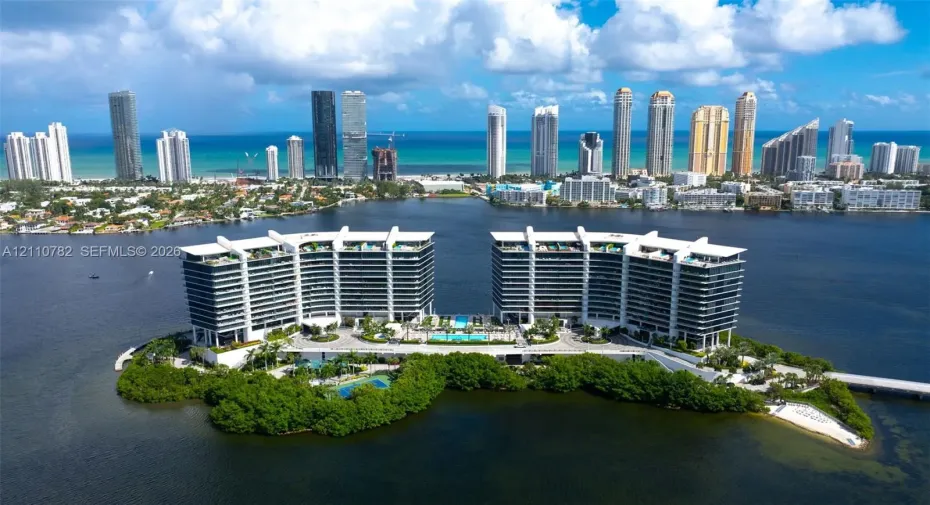 Waterfront high-rise complex situated on a private island, featuring tiered architectural profiles, expansive glass balcony systems, a central outdoor swimming pool, and gated bridge access