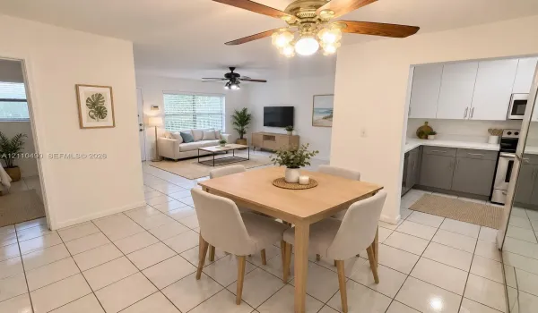 Open-concept interior featuring light-toned tile flooring, dual ceiling fans, and a kitchen equipped with white upper cabinetry and contrasting gray base cabinets