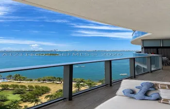 Curved balcony featuring wood-finish flooring and a glass railing with a dark metal frame, overlooking an expansive coastal landscape