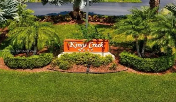 Community signage featuring raised lettering, surrounded by manicured shrubbery, mulch beds, and mature palm trees
