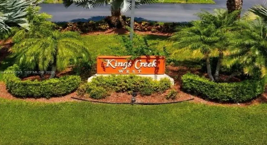 Community signage featuring raised lettering, surrounded by manicured shrubbery, mulch beds, and mature palm trees