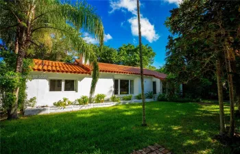 Stucco exterior featuring a terracotta tile roof, multi-pane windows, and a landscaped front yard with mature palms