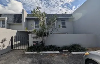 Two-story exterior featuring gray stucco siding, a shingled roof, defined perimeter wall, and private metal gate entry