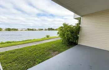 Covered patio featuring concrete flooring, horizontal lap siding, and access to a paved walkway along the water