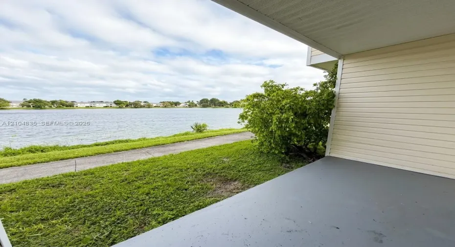 Covered patio featuring concrete flooring, horizontal lap siding, and access to a paved walkway along the water