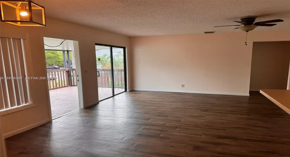 Living area featuring wood-finish flooring, sliding glass doors to a covered deck, pendant lighting, and a ceiling fan