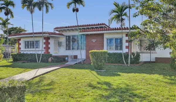Single-story residence featuring a tile roof, brick masonry accents, white stucco exterior, and a paved walkway leading to the entryway