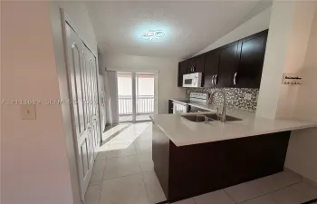 Kitchen featuring dark cabinetry, quartz countertops, mosaic tile backsplash, double-basin stainless steel sink with pull-down faucet, and tile flooring