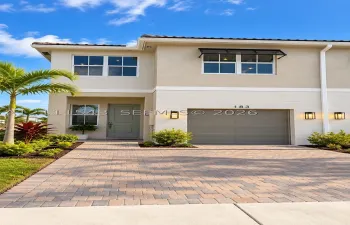 Two-story exterior featuring a neutral stucco and horizontal siding facade, a paver driveway, an attached garage, and exterior wall-mounted lighting
