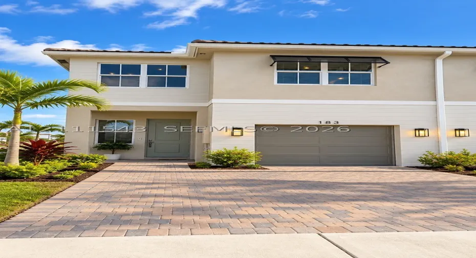 Two-story exterior featuring a neutral stucco and horizontal siding facade, a paver driveway, an attached garage, and exterior wall-mounted lighting