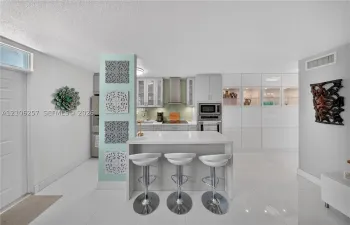 Kitchen featuring a central island with a quartz countertop, white cabinetry, integrated stainless steel appliances, a tile backsplash, and polished tile flooring. Lots of storage!