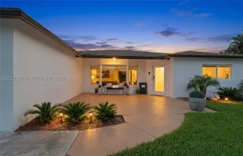 Single-story exterior featuring a smooth stucco finish, a covered concrete patio, a large bay window, and manicured landscaping