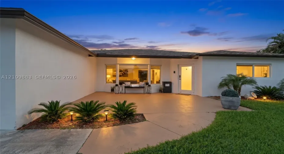 Single-story exterior featuring a smooth stucco finish, a covered concrete patio, a large bay window, and manicured landscaping