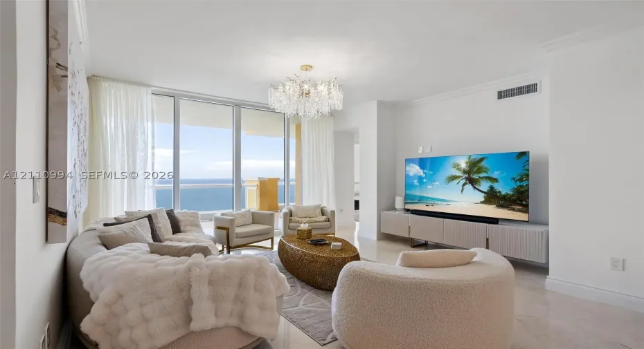 Living space featuring floor-to-ceiling glass panel doors, polished stone flooring, a multi-tiered crystal chandelier, and crown molding