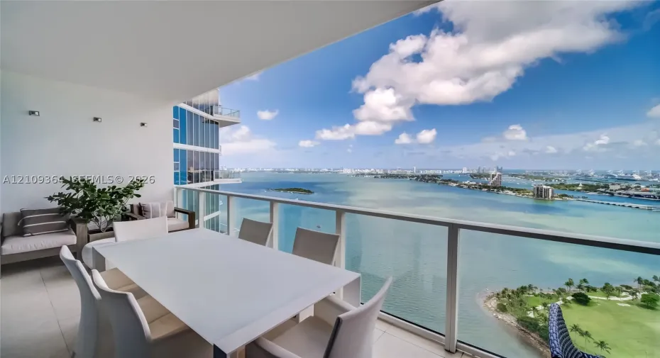 Covered balcony featuring oversized tile flooring, a glass panel railing, and wall-mounted lighting