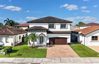 Two-story stucco exterior featuring a multi-hipped tile roof, paver driveway, covered entryway with arched architectural detailing, and a multi-panel garage door