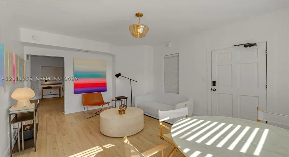 Light-toned wood-finish flooring, gold-toned pendant lighting, multi-panel entry door, and recessed wall alcove