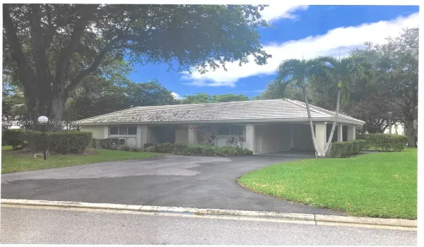 Single-story exterior featuring a gabled roofline, covered entryway, manicured lawn, paved driveway, and mature landscaping