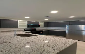 Kitchen featuring charcoal cabinetry with glass-panel accents, stone-composite countertops, stainless steel appliances, and a recessed undermount sink with a high-arch faucet