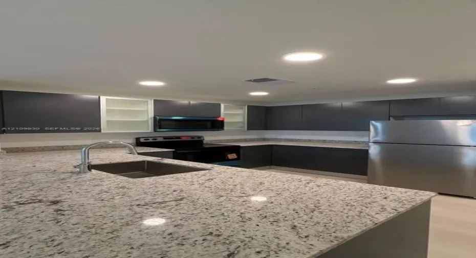 Kitchen featuring charcoal cabinetry with glass-panel accents, stone-composite countertops, stainless steel appliances, and a recessed undermount sink with a high-arch faucet